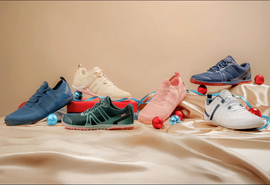 Various styles and colors of Xero barefoot shoes displayed on a draped surface with decorative ornaments.