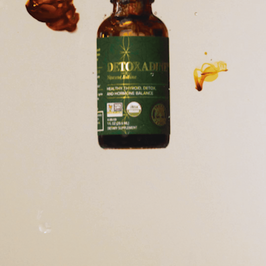 A bottle of Detoxadine nascent iodine supplement, featuring a green label with text indicating it's for healthy thyroid, detox, and hormone balance, with some liquid splashed nearby.